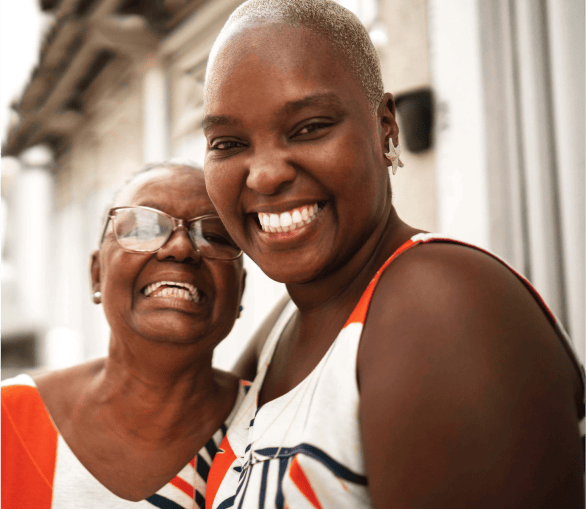 An elderly parent embracing her daughter, both smiling at the camera happily